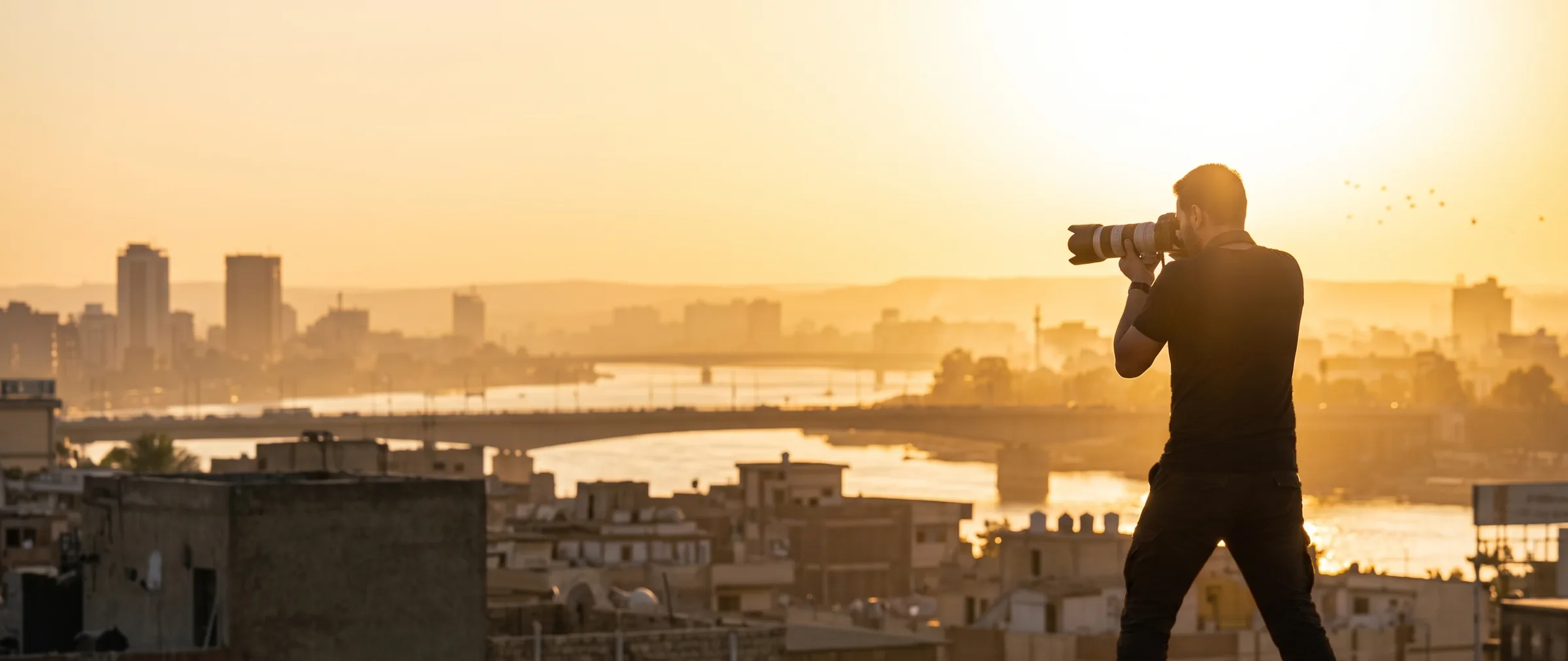 Fotograaf met telelens legt vanaf een dak een stad vast bij zonsopgang